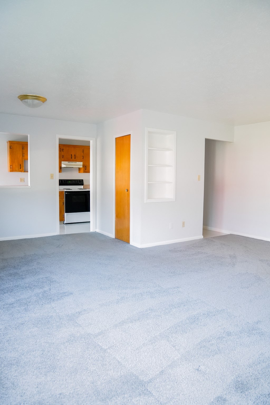 an empty living room with a white carpet and a kitchen
