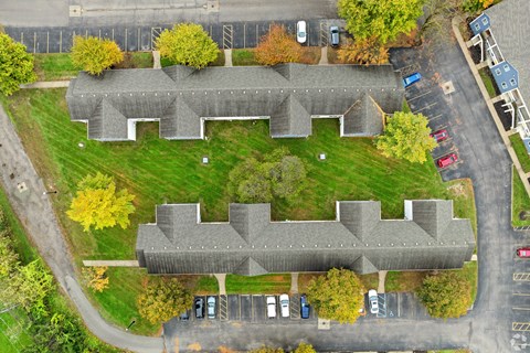 An aerial view of a grey building surrounded by a parking lot and trees.