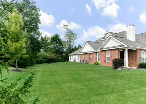 A house with a red brick exterior and a white roof is surrounded by a green lawn and trees.