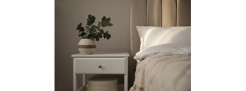 A white table with a plant on it sits next to a bed.