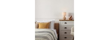 A bed with a yellow pillow and a grey blanket is in front of a white wall.