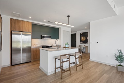 A modern kitchen with a white island and wooden chairs.