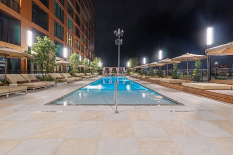 A large outdoor swimming pool surrounded by a tiled floor and lounge chairs.