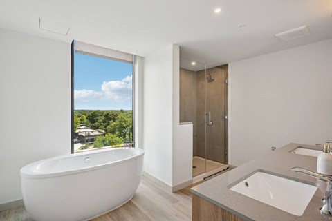 A white bathroom with a large window and a white bathtub.