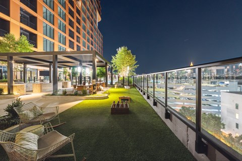 A rooftop patio with a table and chairs overlooking a city at night.