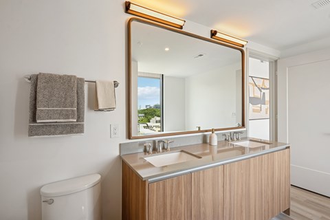 A bathroom with a white toilet and a wooden vanity with a mirror above it.