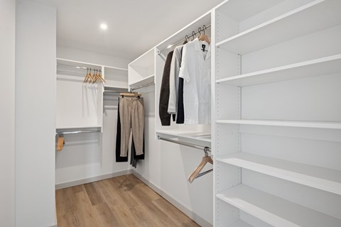 A white walk in closet with clothes hanging on hangers.