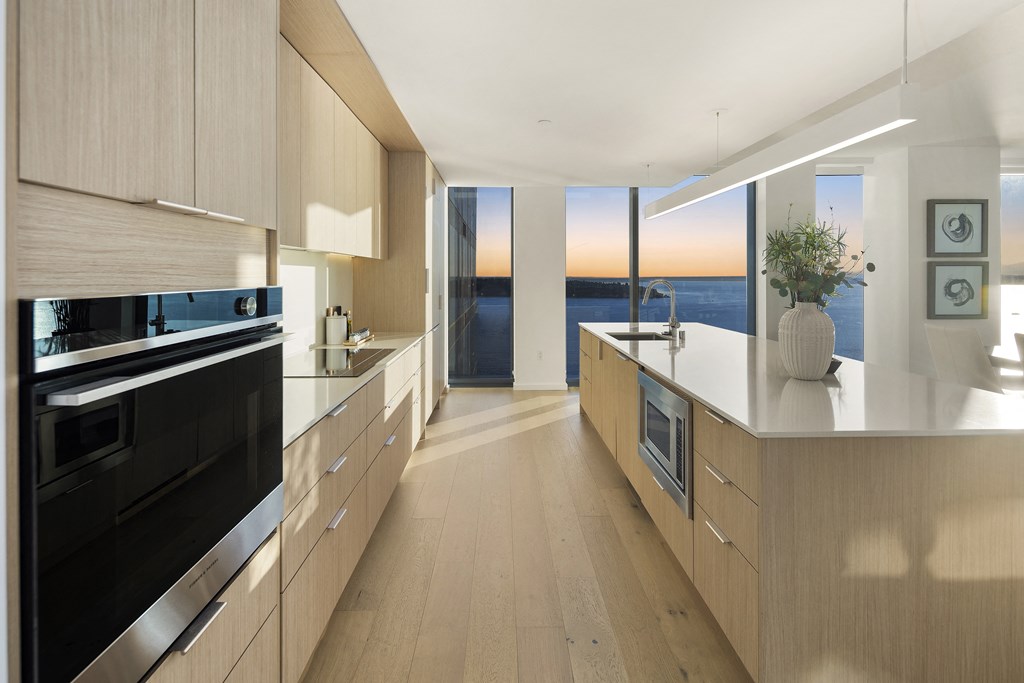 a kitchen with wooden cabinets and white countertops with a view of the ocean in the distance