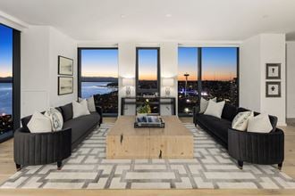 a living room with black couches and a wooden coffee table with a view of the city
