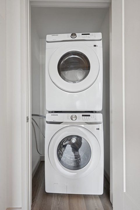 A white washing machine is stacked on top of another white washing machine in a small laundry room.