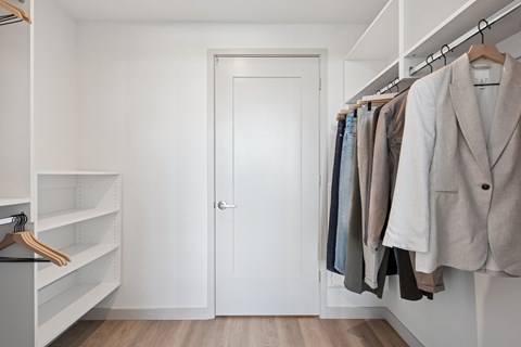 A white closet with clothes hanging and a white door.