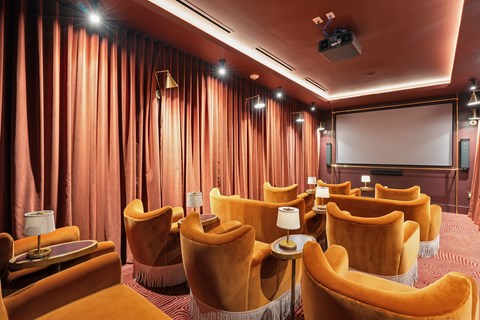A cinema room with orange chairs and a screen.