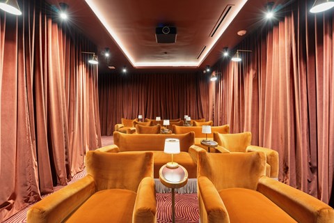 A cinema room with orange chairs and curtains.