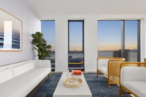 A living room with a white sofa, a wooden chair, and a coffee table in front of a window with a view of the city.