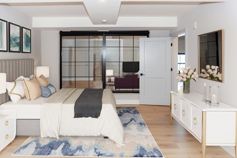 A bedroom with a bed, nightstand, and a large window with a view of a balcony.