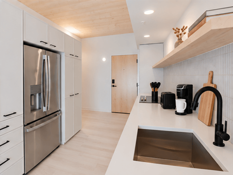 A modern kitchen with a stainless steel refrigerator and a wooden shelf above the sink.