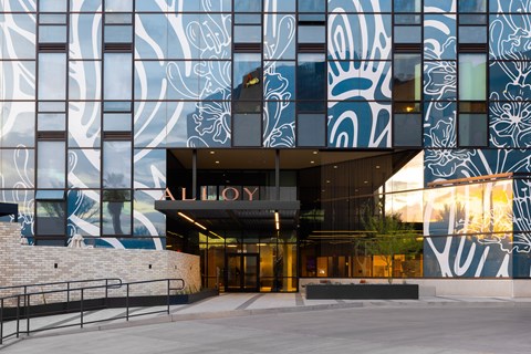 The Alloy building has a modern design with a glass facade and a large mural on the side.