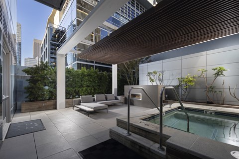A hot tub is surrounded by a cushioned seating area on a rooftop patio.