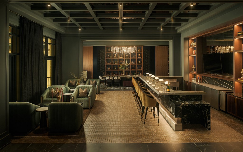 A well-lit, modern bar area with a long counter and green armchairs.