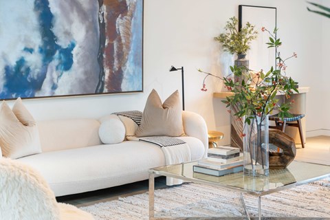 A living room with a white couch and a painting on the wall.