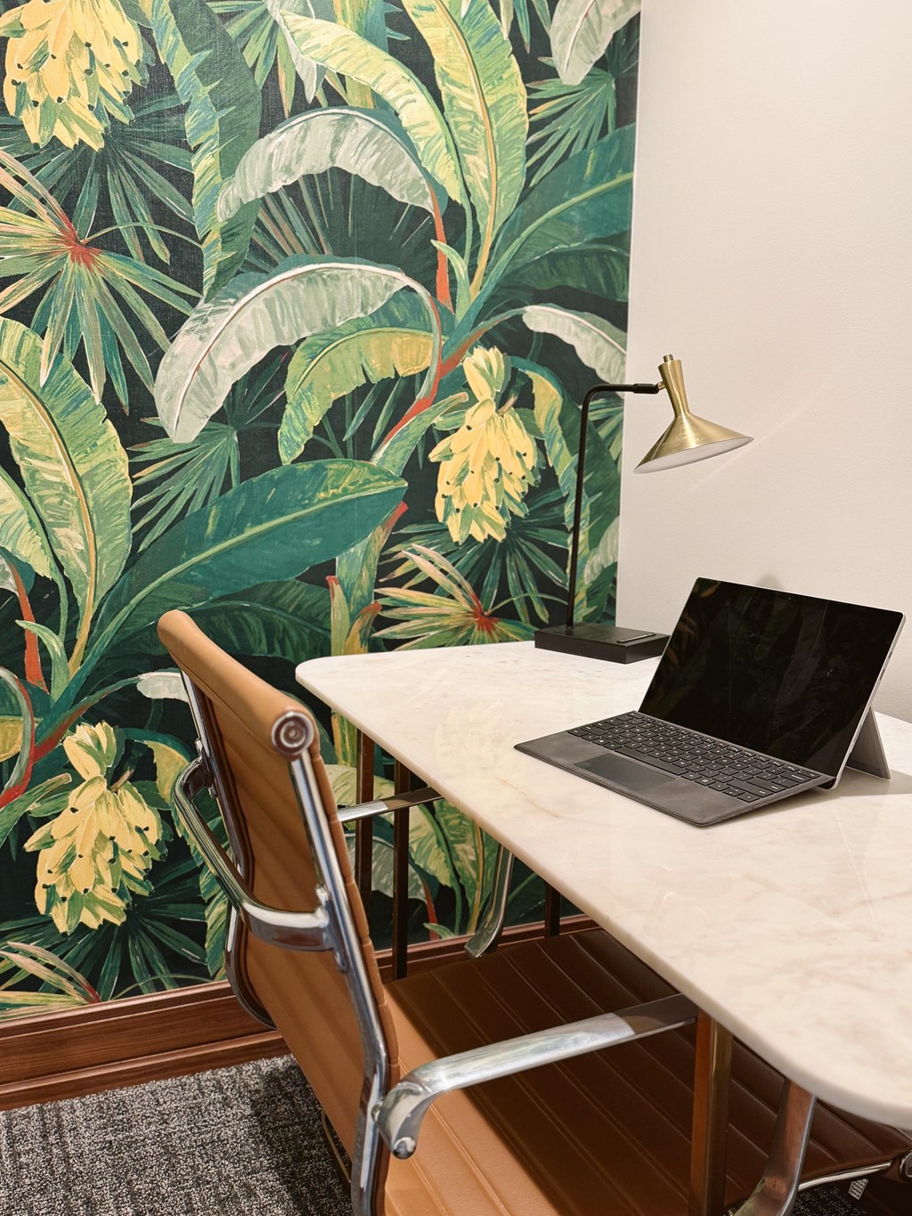 A laptop is on a desk in front of a wallpapered wall.