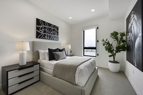 A bedroom with a large bed, a nightstand with two lamps, and a plant in a white pot.