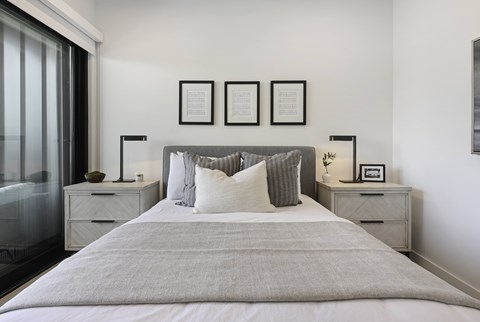 A bedroom with a large bed, two nightstands, and framed pictures on the wall.