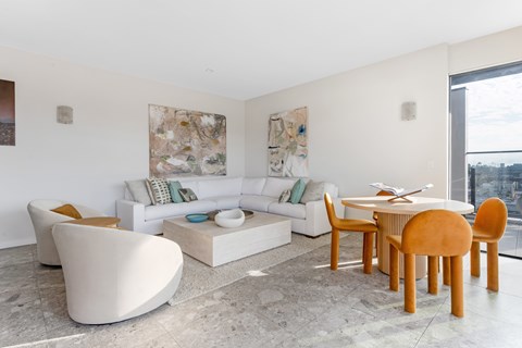 A modern outdoor rooftop living room with a white sofa, a round table, and a large abstract painting on the wall.