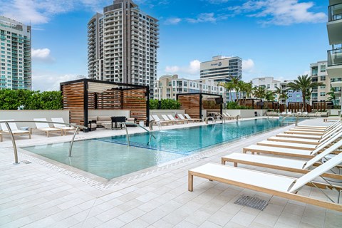 A pool area with sun loungers and a building in the background.