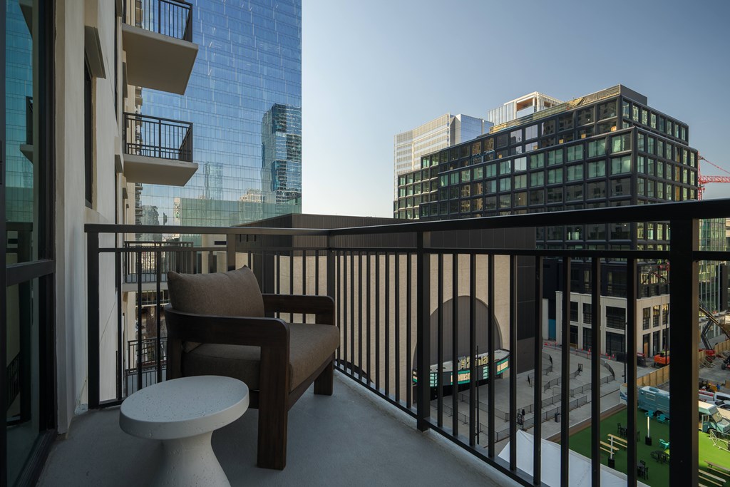 A balcony with a chair and table overlooking a cityscape.