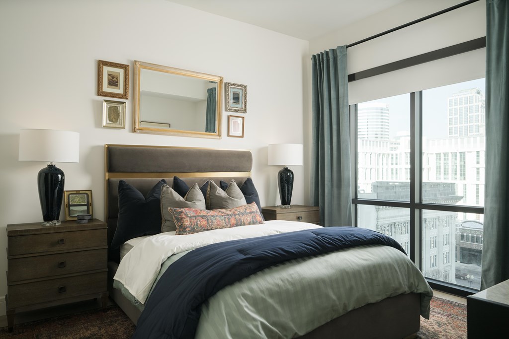 A bedroom with a large bed, a mirror, and a window overlooking a cityscape.