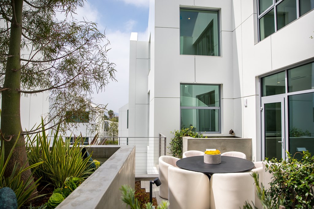 a patio with a round table and white chairs in front of a white building