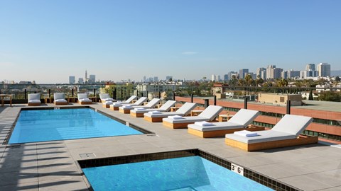 A pool with sun loungers and a city skyline in the background.