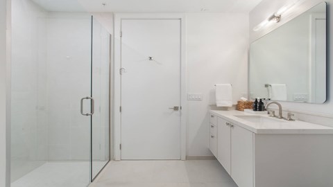 A white bathroom with a sink, mirror, and shower.