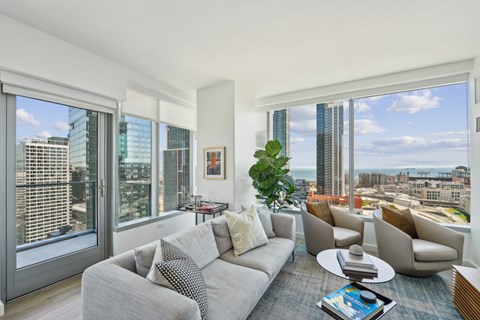A living room with a grey couch and a large window overlooking the city.