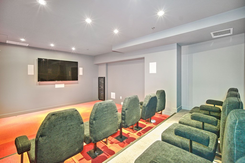A row of green chairs are arranged in a room with a television on the wall.