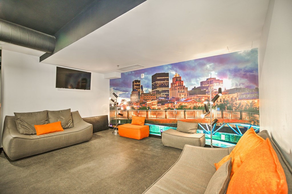A living room with a grey couch and orange pillows.
