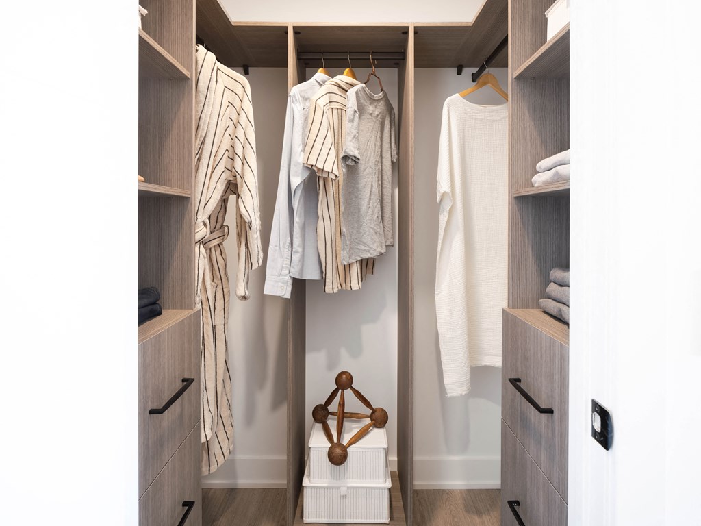 a walk in closet with white clothes and wooden hangers