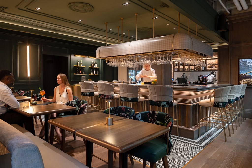 a woman sitting at a table in a restaurant with a bartender behind the bar