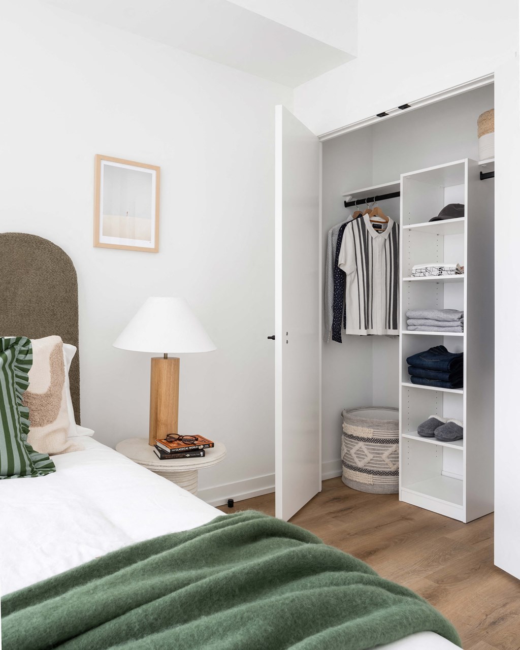 A white bedroom with a green blanket on the bed.