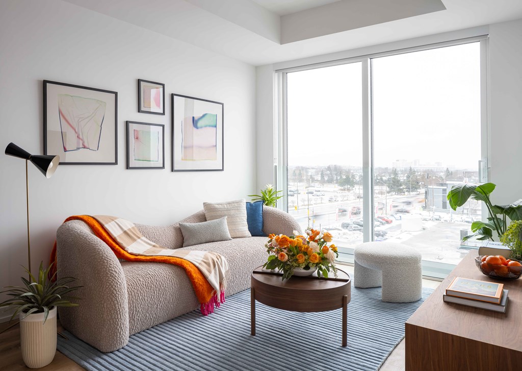 A living room with a couch, a table, and a window overlooking a parking lot.