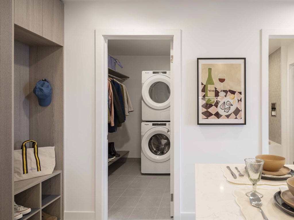 A laundry room with a washer and dryer, a shelf with bags and a painting on the wall.
