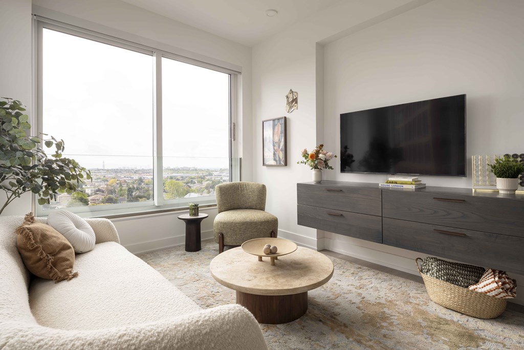 A living room with a large window, a sofa, a chair, a coffee table, and a TV.