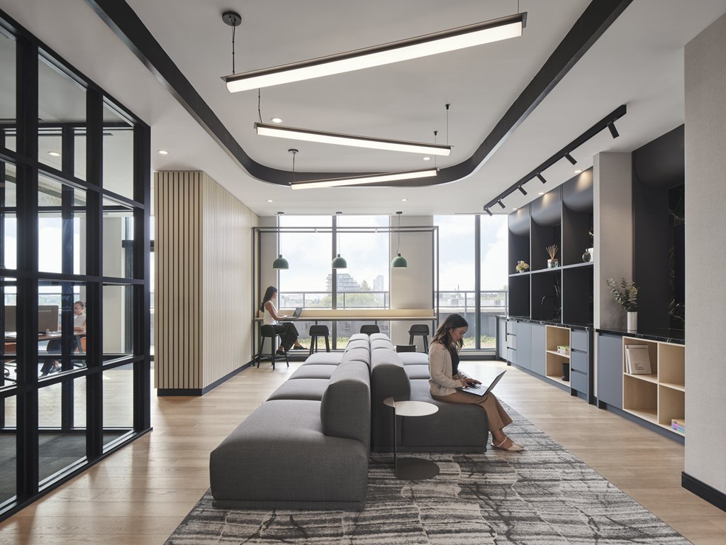 A woman is sitting on a grey sofa in a modern room with a large window.