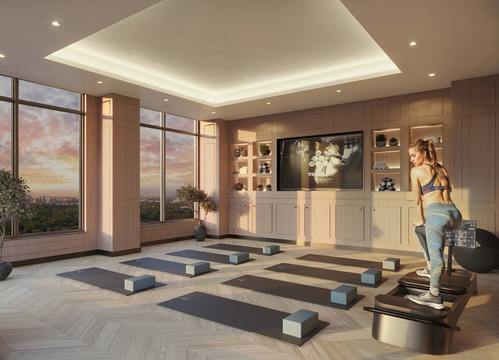 A woman is exercising on a treadmill in a spacious room with yoga mats and a view of the city.