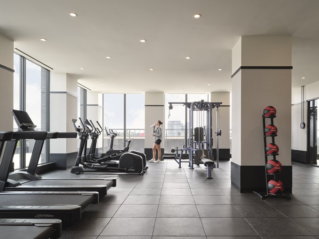 A woman is working out in a gym with treadmills, elliptical machines, and other exercise equipment.