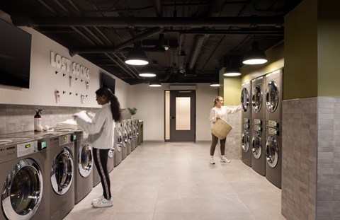 A woman is standing in front of a row of washing machines in a laundromat.
