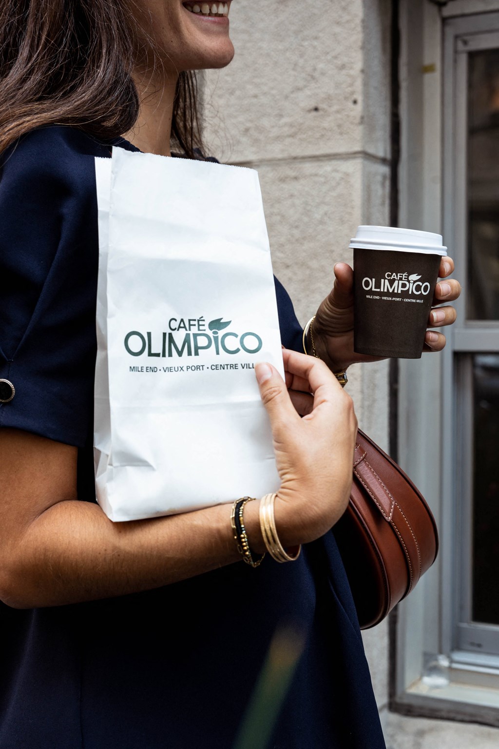 a woman holding a cup of coffee and a bag of cafe olimpicco