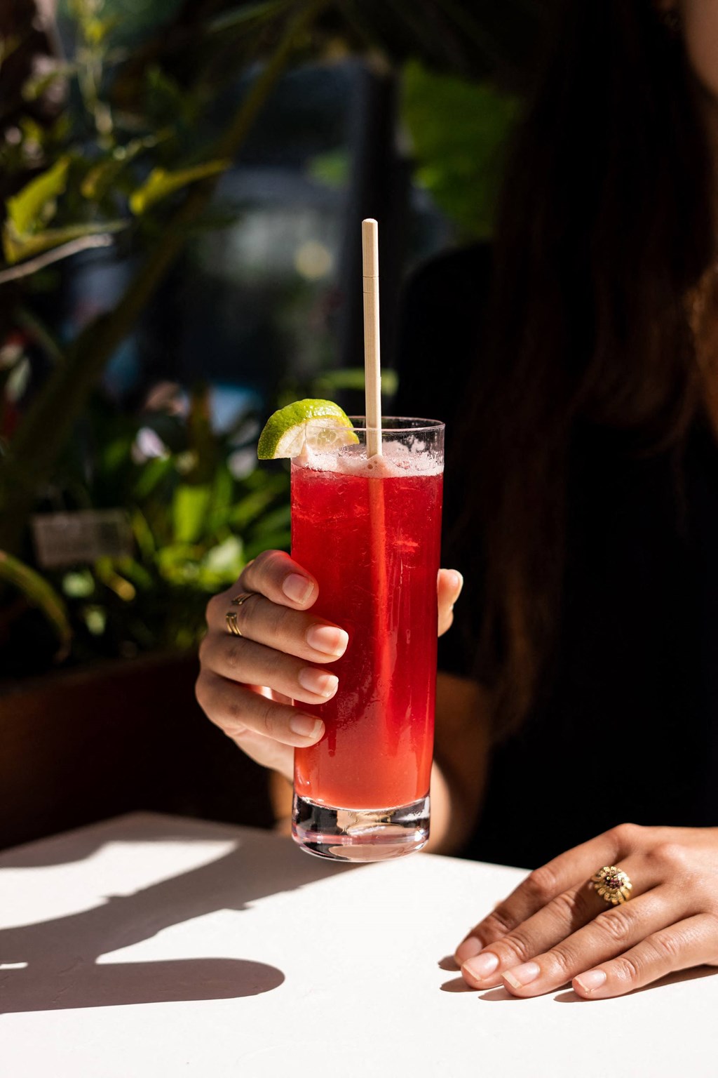 a woman holding a red cocktail in a glass with a straw
