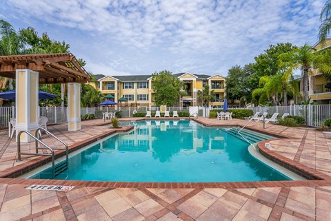 A large swimming pool surrounded by a tiled patio and lounge chairs.
